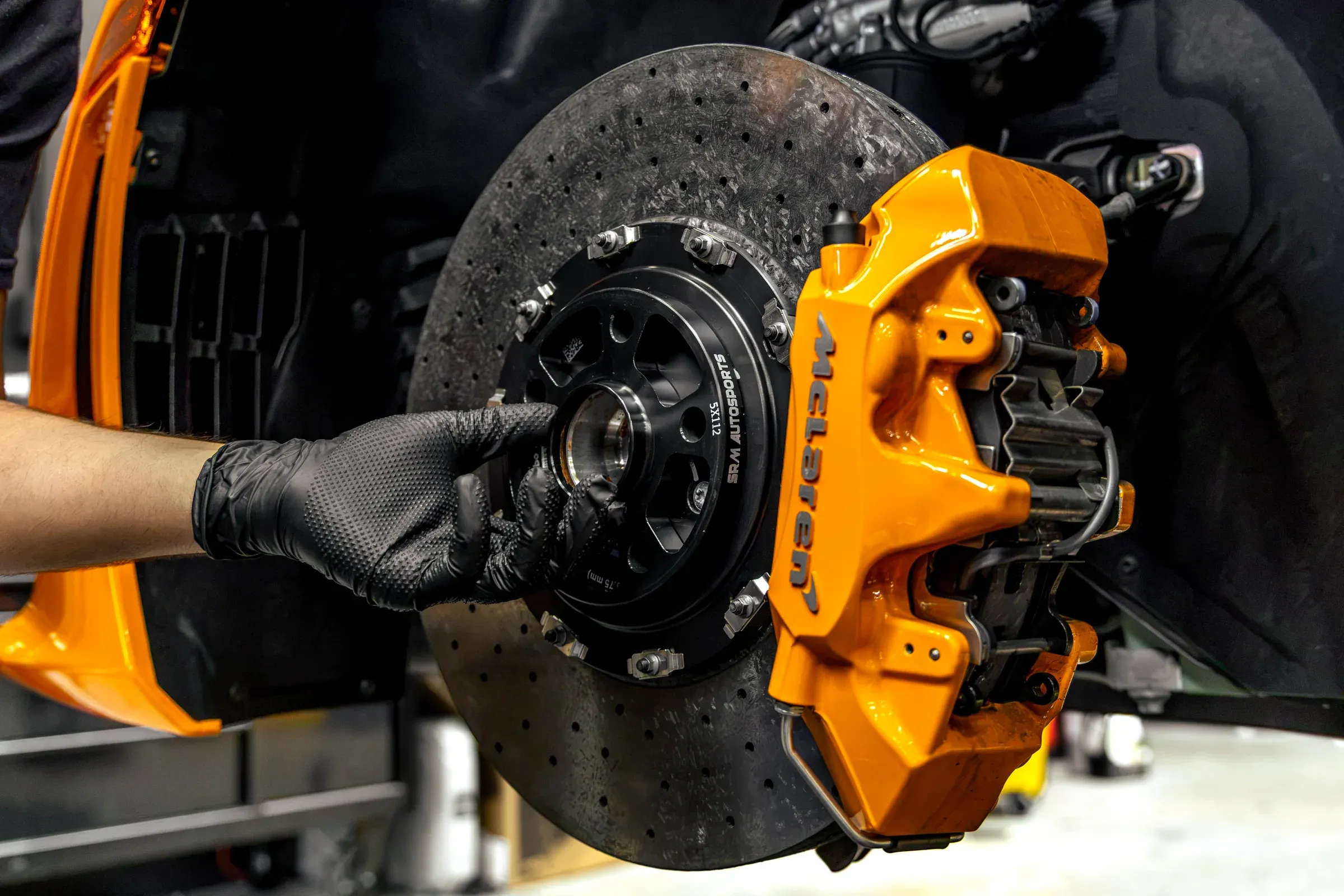 Technician servicing the carbon-ceramic brake assembly of an orange McLaren